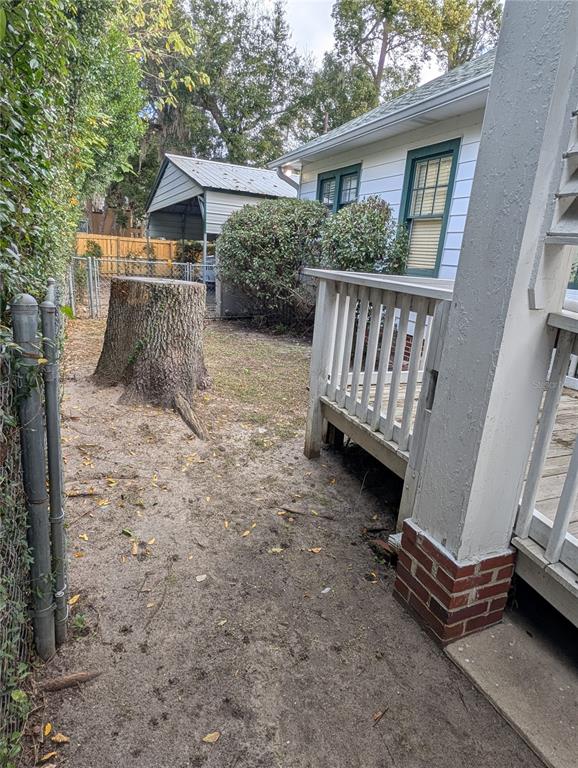 A backyard view featuring a large tree stump, a wooden deck, and a metal carport — 1427 E FORT KING STREET, OCALA, FL