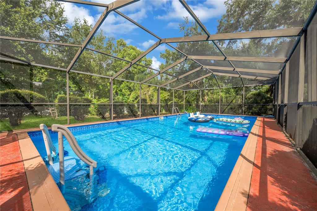 A rectangular swimming pool with a screen enclosure and pool floats on a sunny day — 1708 WOODBINE DRIVE, BRANDON, FL
