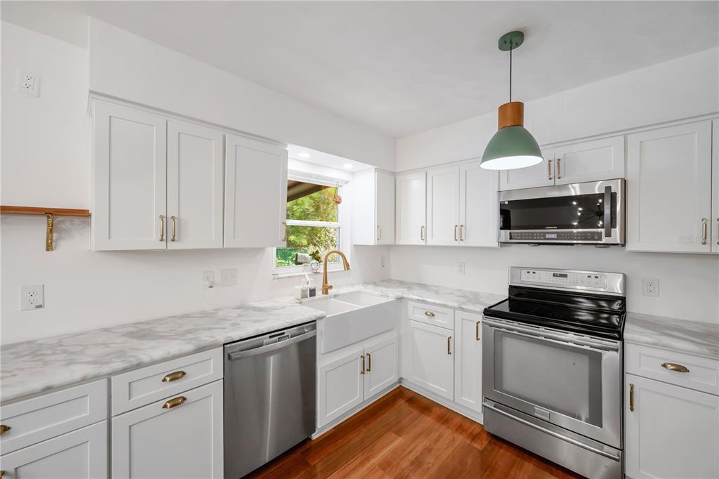A kitchen with white cabinets, marble-look countertops, stainless steel appliances, and a farmhouse sink — 1708 WOODBINE DRIVE, BRANDON, FL