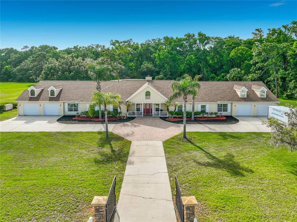 A yellow, single-story house with a paved driveway, palm trees, and a central front entrance — 2300 PINE MEADOWS PLACE, CHULUOTA, FL