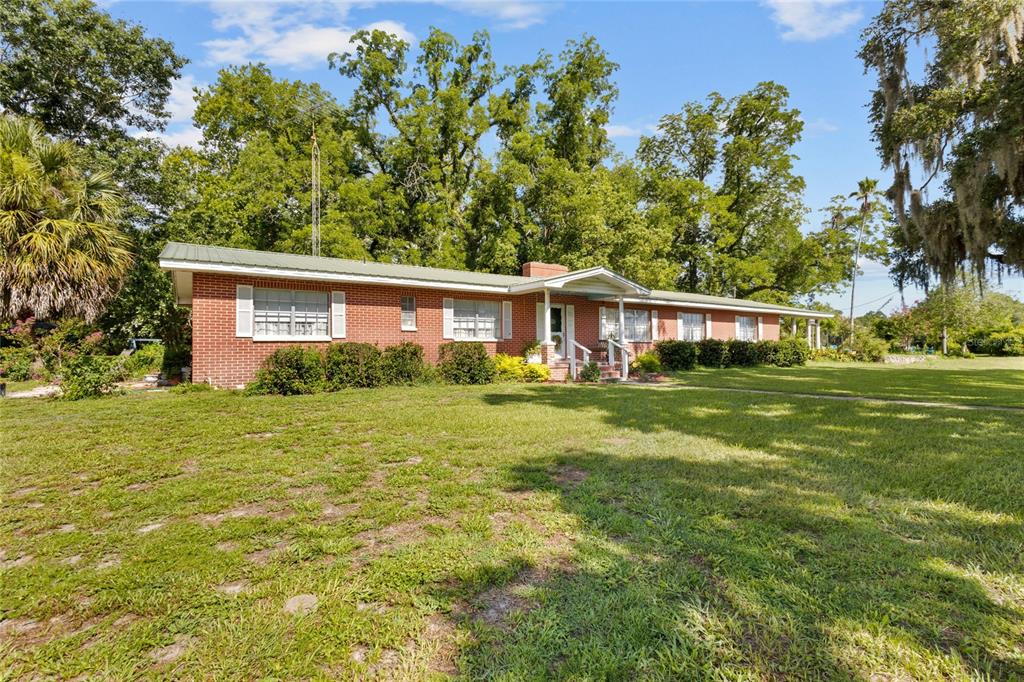 A single-story red brick house with a metal roof sits on a grassy lot — 18951 SE 15TH STREET, WILLISTON, FL