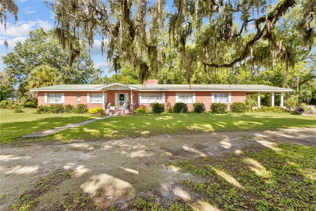 A single-story red brick house with a metal roof sits on a grassy lot — 18951 SE 15TH STREET, WILLISTON, FL