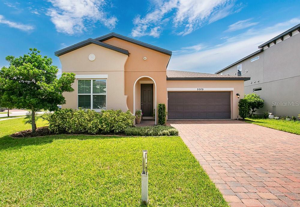 A single-story house with a tan stucco exterior, a brick driveway, and a two-car garage — 2009 NAPOLI DRIVE, ST CLOUD, FL