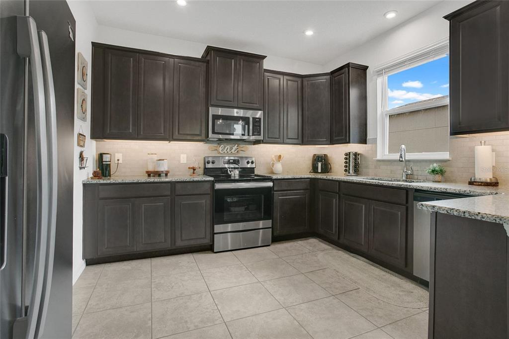A kitchen features dark wood cabinets, stainless steel appliances, granite countertops, and light tile flooring — 2009 NAPOLI DRIVE, ST CLOUD, FL