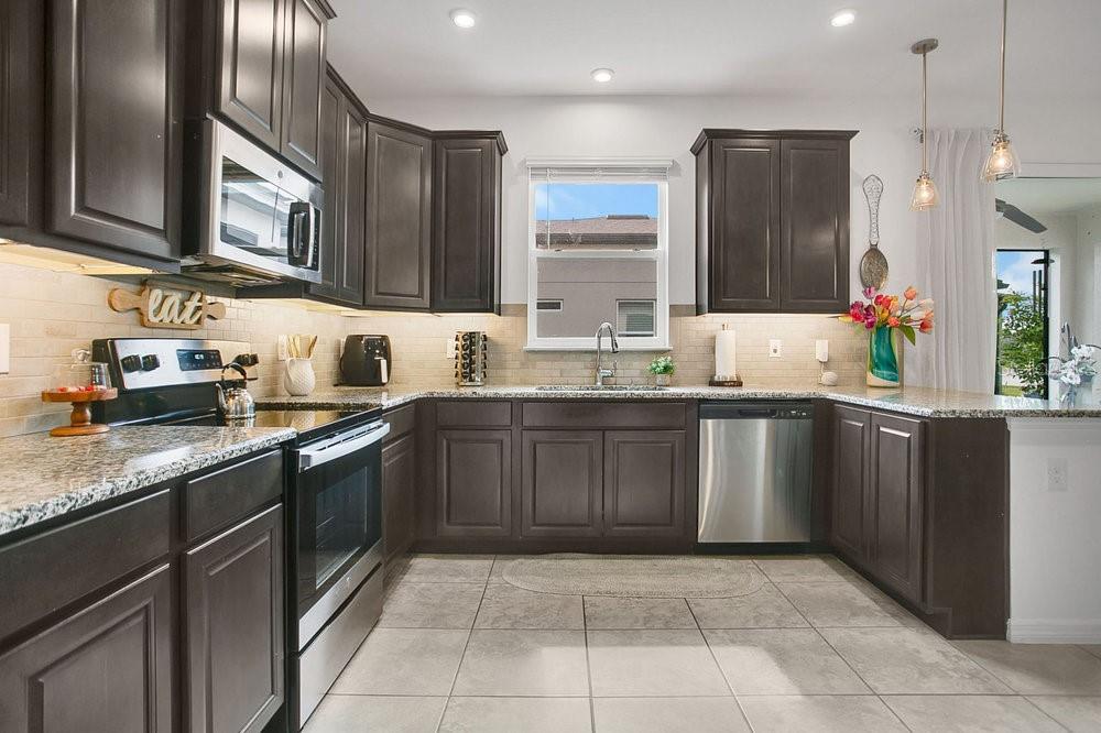 A kitchen with dark wood cabinets, stainless steel appliances, granite countertops, and tile flooring — 2009 NAPOLI DRIVE, ST CLOUD, FL