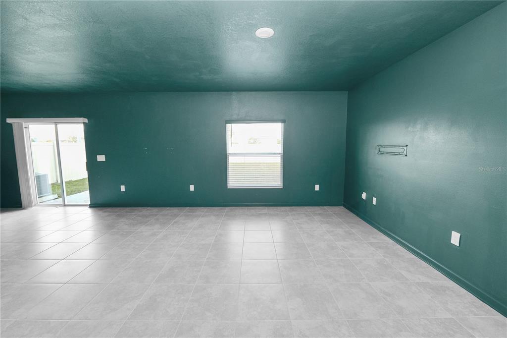 An empty room features dark teal walls, light gray tile flooring, and a sliding glass door — 1465 DEEPWATER CIRCLE, EAGLE LAKE, FL