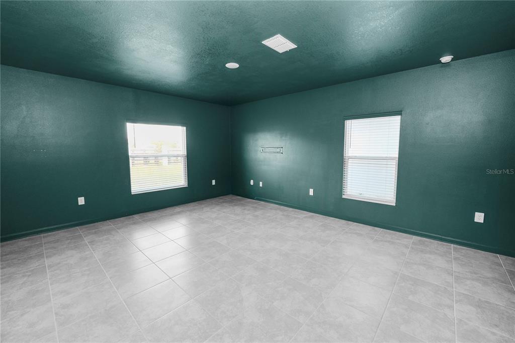 An empty room features dark green walls, light gray tile flooring, and two windows — 1465 DEEPWATER CIRCLE, EAGLE LAKE, FL