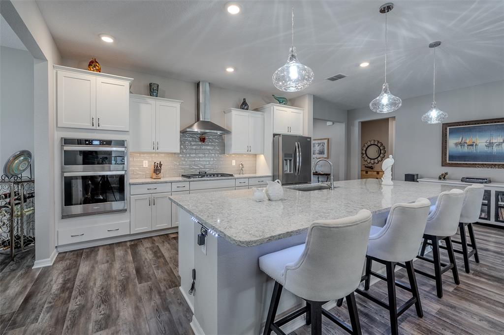 A modern kitchen features white cabinetry, a large granite island, and stainless steel appliances — 10586 SW 98TH PLACE, OCALA, FL