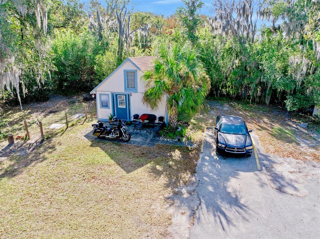 A small, light-colored cottage with a blue door sits next to a motorcycle and car — 228 W HOWRY AVENUE, DELAND, FL