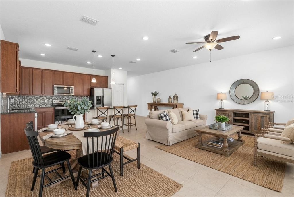 An open-concept living and dining area features wood cabinets, a kitchen island, and neutral furniture — 3 OAKLEAF WAY, PALM COAST, FL
