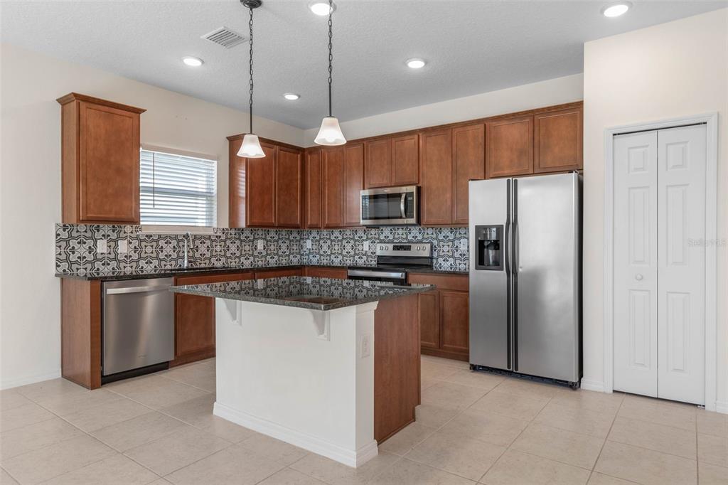 A kitchen features wood cabinets, stainless steel appliances, a patterned backsplash, and a central island — 3 OAKLEAF WAY, PALM COAST, FL