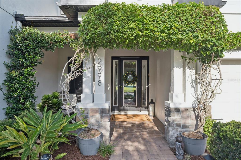 A covered front entryway features stone pillars, a brick walkway, and lush climbing greenery — 2998 RIDERS PASS, ODESSA, FL