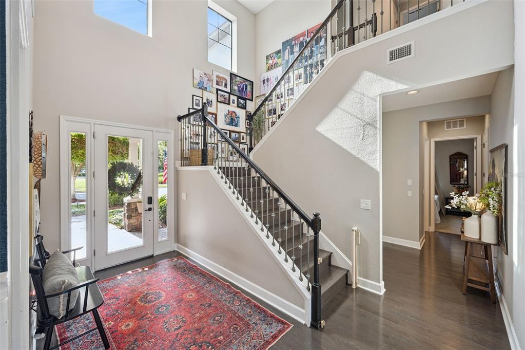 A bright foyer features a staircase with black railings, a red rug, and hardwood floors — 2998 RIDERS PASS, ODESSA, FL