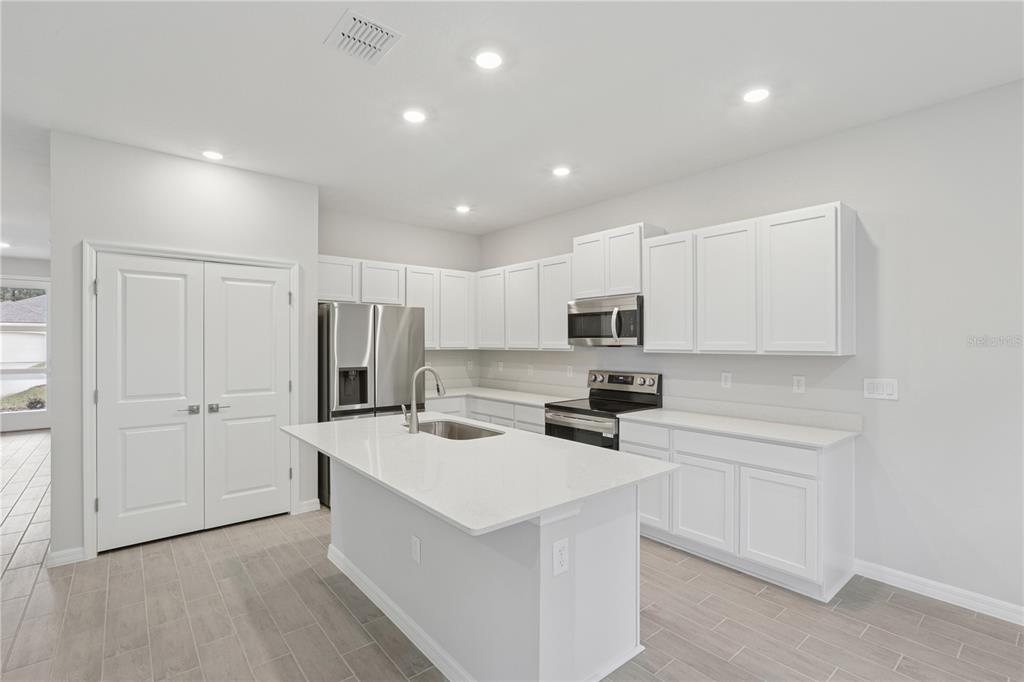 A modern kitchen features white cabinets, a central island, stainless steel appliances, and tile flooring — 17094 SW 20TH CT ROAD, OCALA, FL