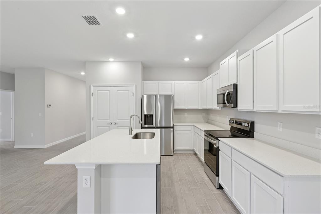 A modern kitchen features white cabinets, stainless steel appliances, a quartz island, and tile flooring — 17094 SW 20TH CT ROAD, OCALA, FL