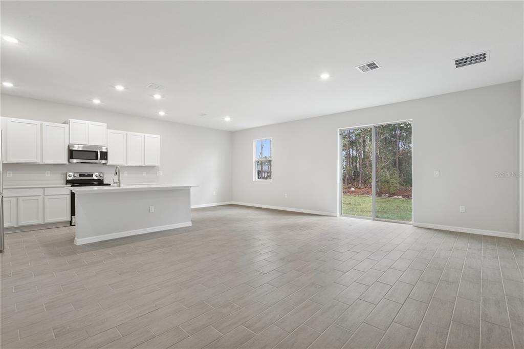 An open-concept kitchen and living area with white cabinets, stainless appliances, and tile flooring — 17094 SW 20TH CT ROAD, OCALA, FL