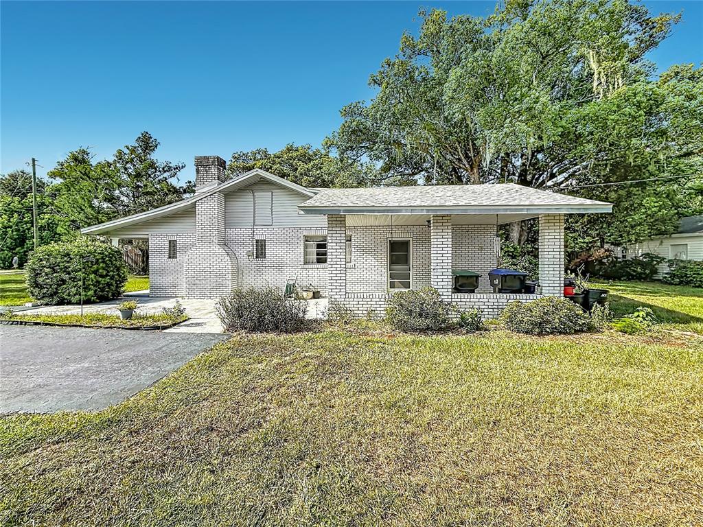 A white brick house features a covered front porch and a large shade tree — 3271 ROBINSON STREET, ZELLWOOD, FL