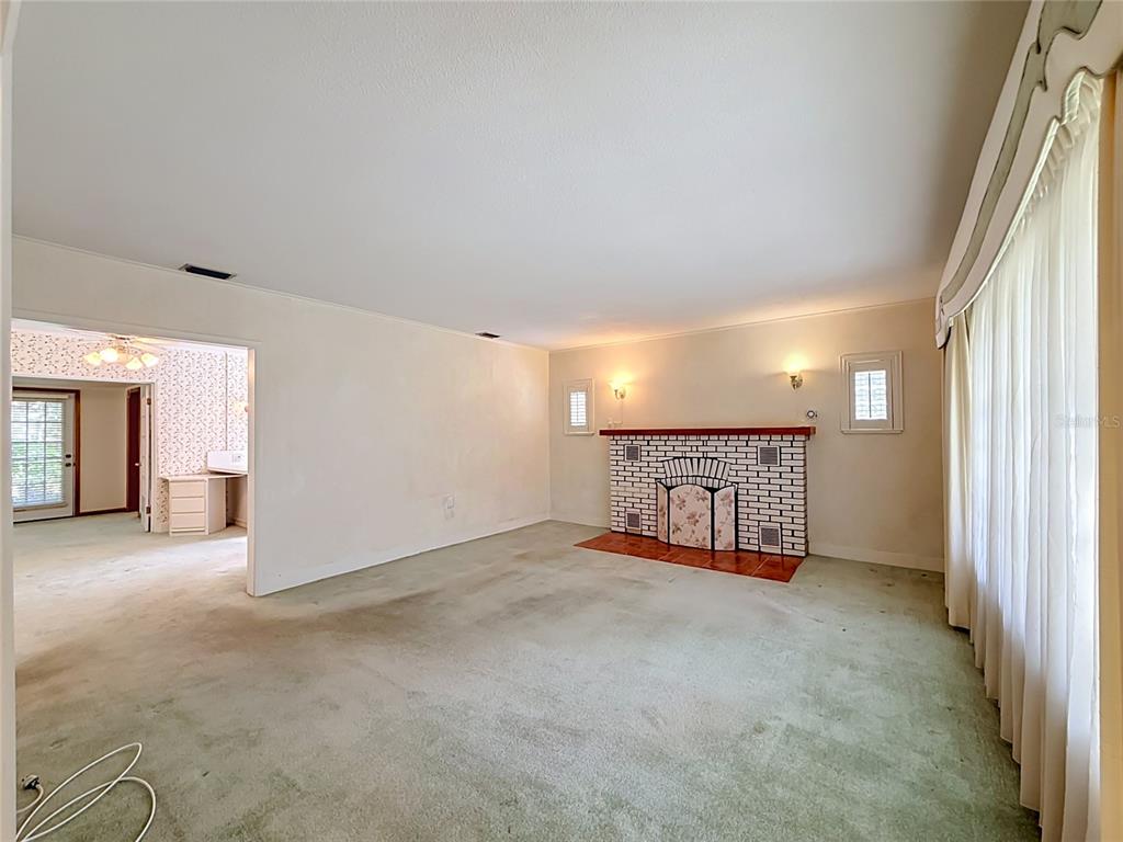 A living room with green carpet, a white brick fireplace, and an adjacent room entrance — 3271 ROBINSON STREET, ZELLWOOD, FL
