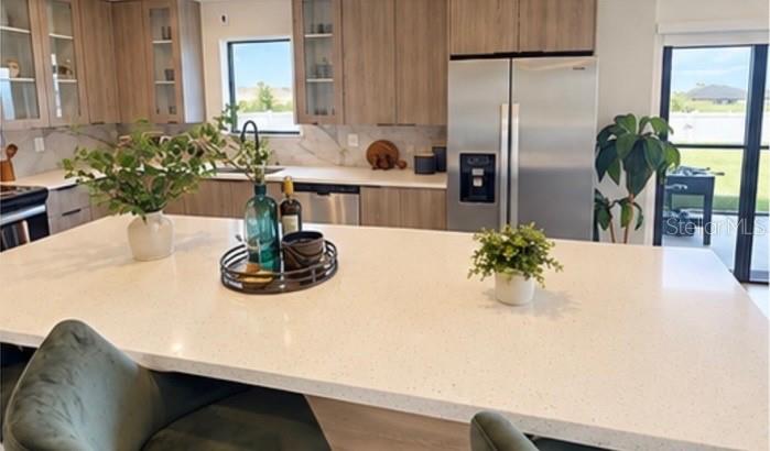 A modern kitchen features light wood cabinets, a large quartz island, and stainless steel appliances — 6471 CHORUS DRIVE, MASCOTTE, FL