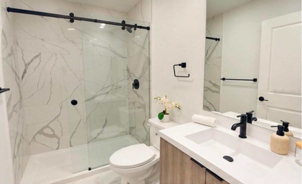A modern bathroom features a marble-tiled shower, a wood vanity, and matte black hardware — 6471 CHORUS DRIVE, MASCOTTE, FL