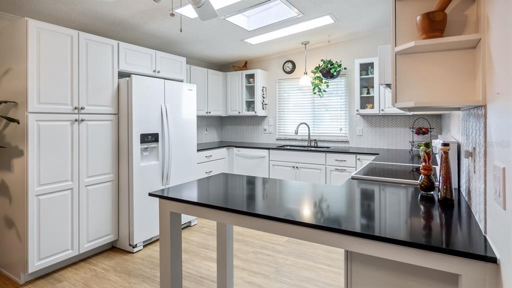 A kitchen features white cabinetry, black countertops, a white refrigerator, and a herringbone backsplash — 3109 MANATEE ROAD, TAVARES, FL