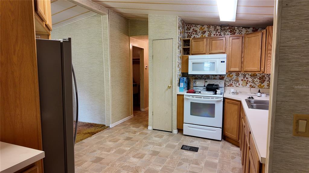 A kitchen with wood cabinets, white appliances, patterned wallpaper, and light-colored vinyl flooring — 4641 A STREET, ST CLOUD, FL