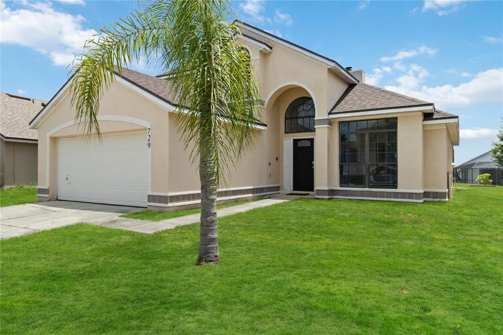 A single-story stucco house with a two-car garage, a palm tree, and a front entrance — 729 DOWNING CIRCLE, DAVENPORT, FL
