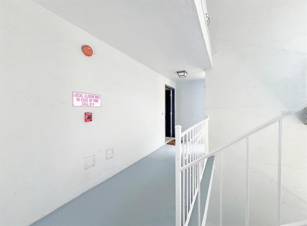 An outdoor apartment hallway features white walls, a gray floor, and a metal railing — 8203 OLYMPIA COURT, LONGWOOD, FL