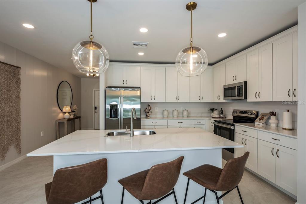 A modern kitchen features white cabinetry, a large quartz island, and two glass pendant lights — 9505 VIBRANT LANE, VENICE, FL