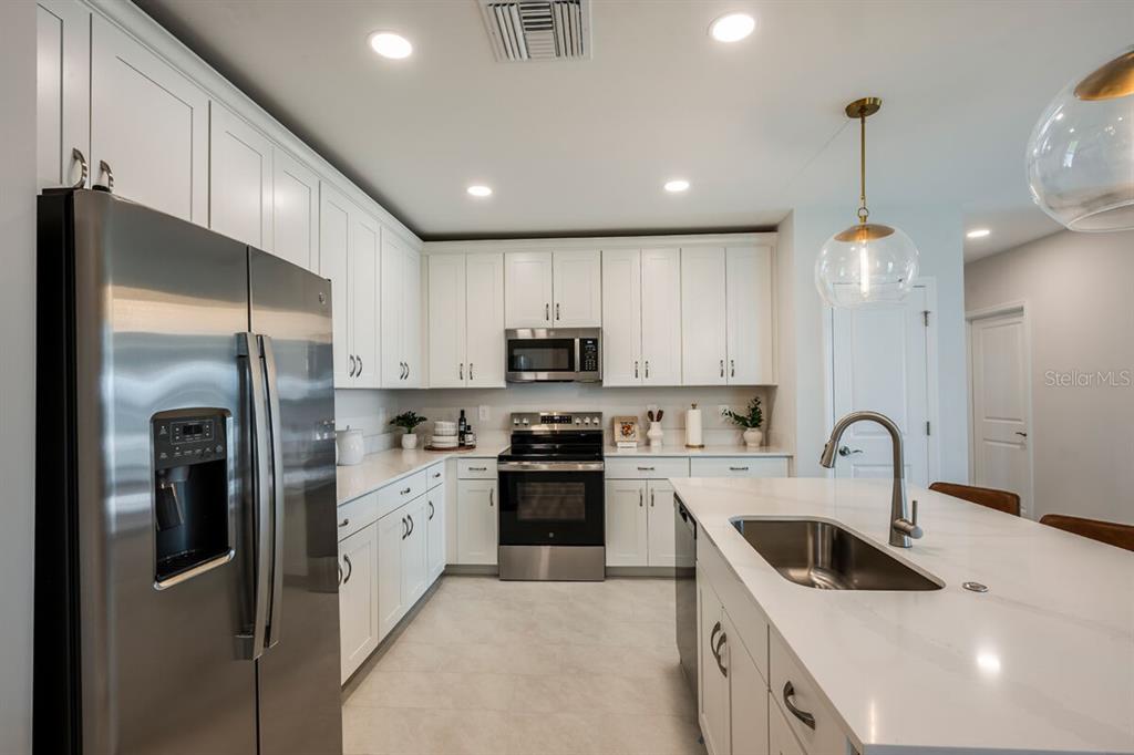 A modern kitchen features white cabinets, stainless steel appliances, and a large quartz-topped island — 9505 VIBRANT LANE, VENICE, FL