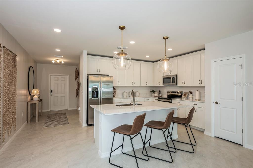 A modern kitchen features white cabinetry, a central island with three stools, and stainless appliances — 9505 VIBRANT LANE, VENICE, FL