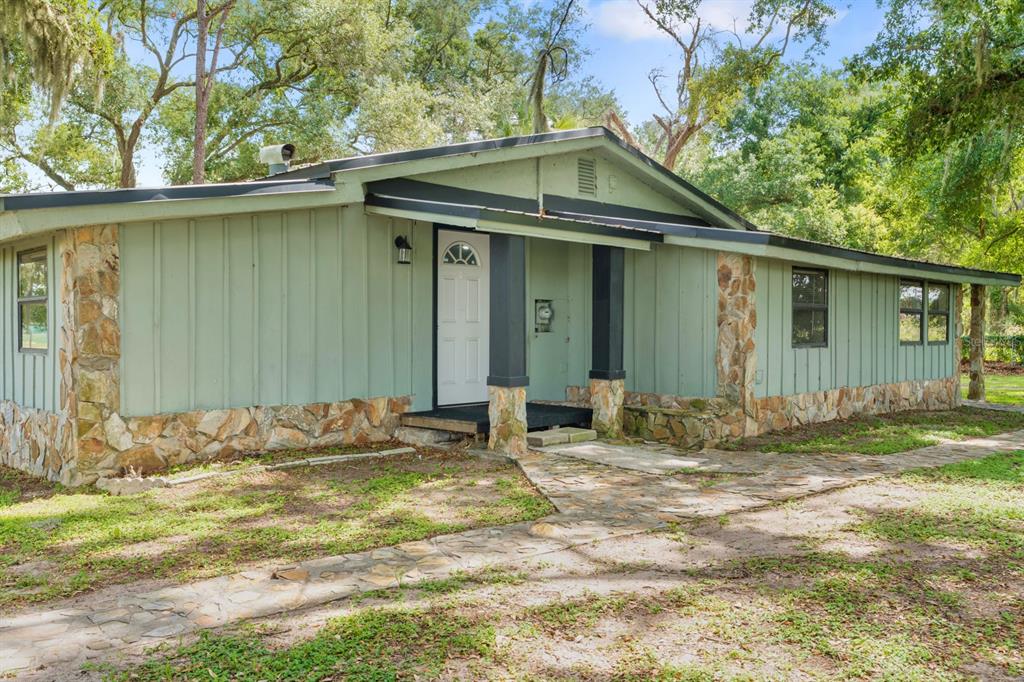 A single-story house with green vertical siding, stone accents, and a stone walkway — 12616 THONOTOSASSA ROAD, THONOTOSASSA, FL