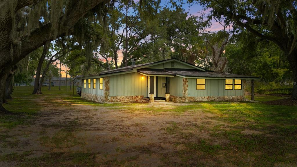 A single-story house with light green vertical siding and stone accents sits among trees — 12616 THONOTOSASSA ROAD, THONOTOSASSA, FL