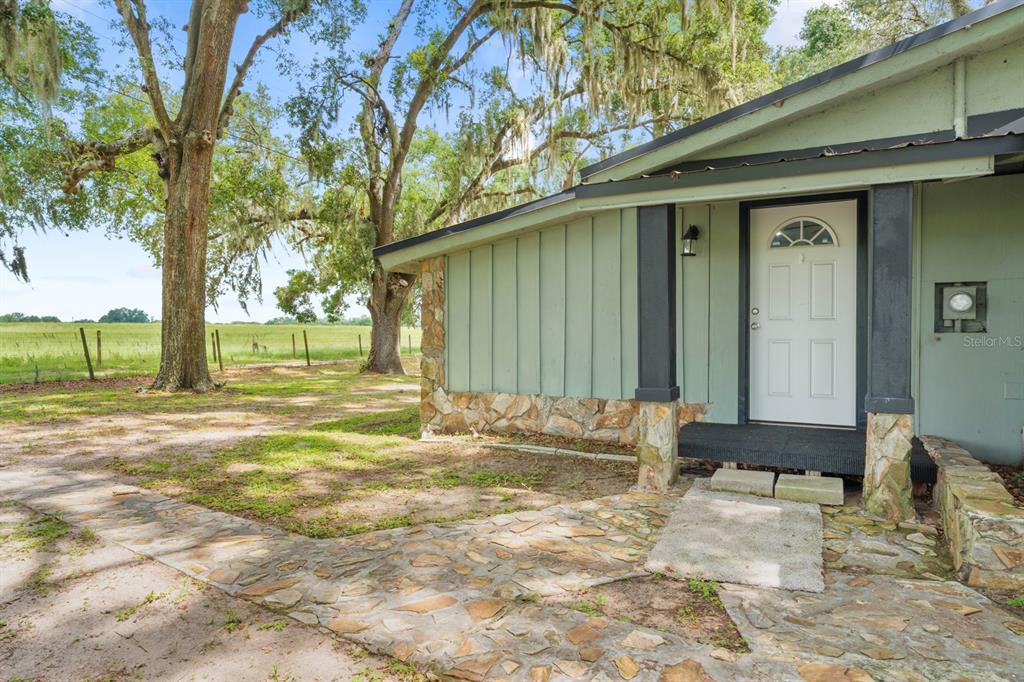 A green house with stone accents and a white front door sits near large trees — 12616 THONOTOSASSA ROAD, THONOTOSASSA, FL