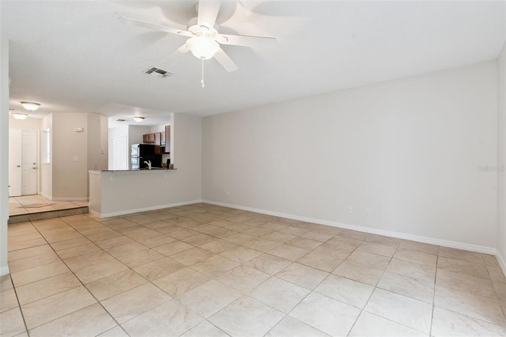 An empty living room with beige tile flooring, a ceiling fan, and an open kitchen — 679 CLEMSON DRIVE, ALTAMONTE SPRINGS, FL