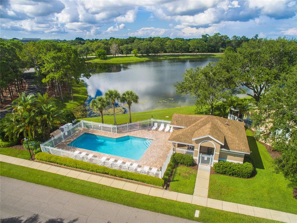 An aerial view shows a swimming pool and clubhouse beside a lake surrounded by trees — 1937 NORTHFORK CIRCLE, CLEARWATER, FL