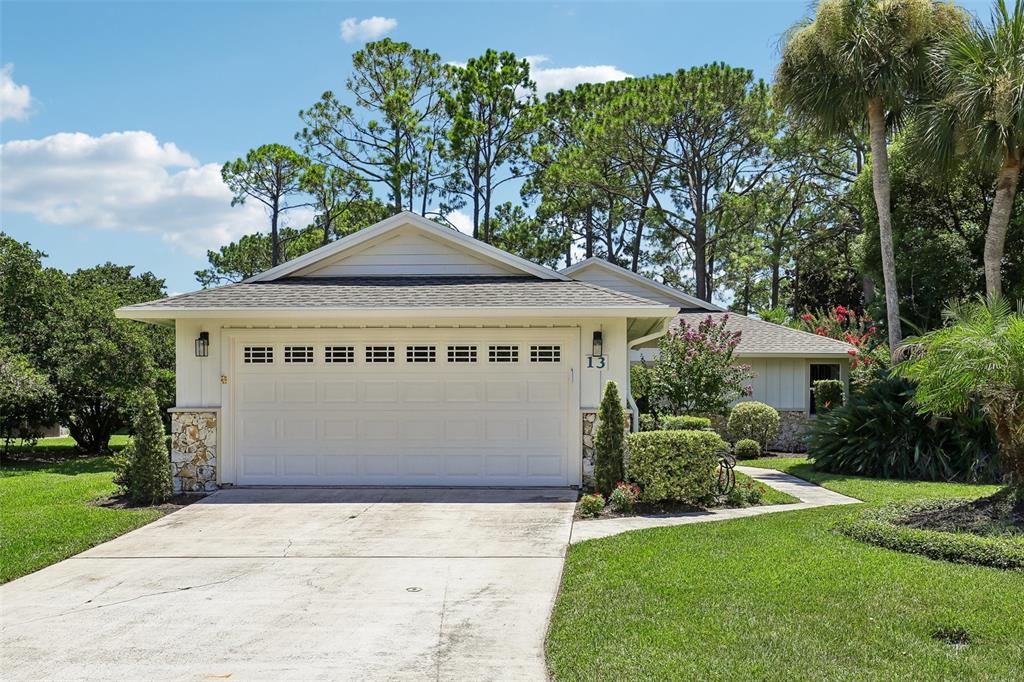 A single-story house with a white garage door, stone accents, and a landscaped front yard — 13 JASMINE RUN, ORMOND BEACH, FL