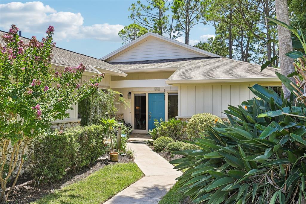 A concrete walkway leads to the blue front door of a single-story house with landscaping — 13 JASMINE RUN, ORMOND BEACH, FL