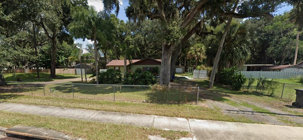 A single-story house with a brown roof sits behind a chain-link fence and large trees — 1828-1840 PROVIDENCE ROAD, BRANDON, FL