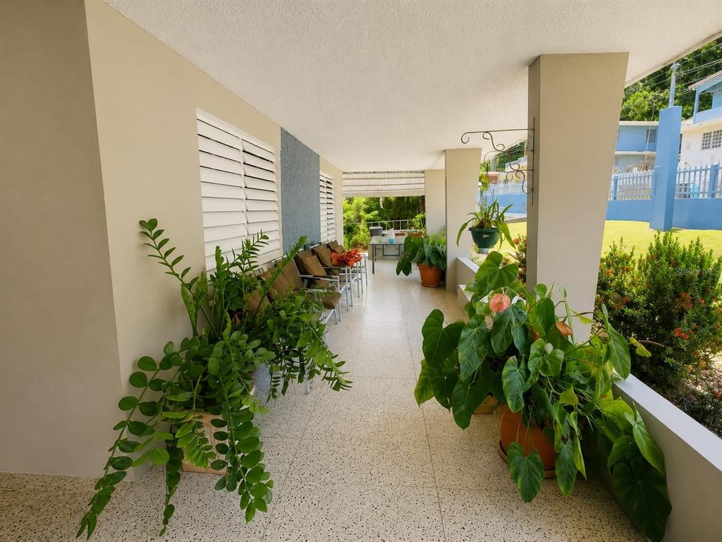 A covered outdoor patio features tiled flooring, potted plants, and a row of chairs — 2.2 677 ROAD, VEGA ALTA, PR