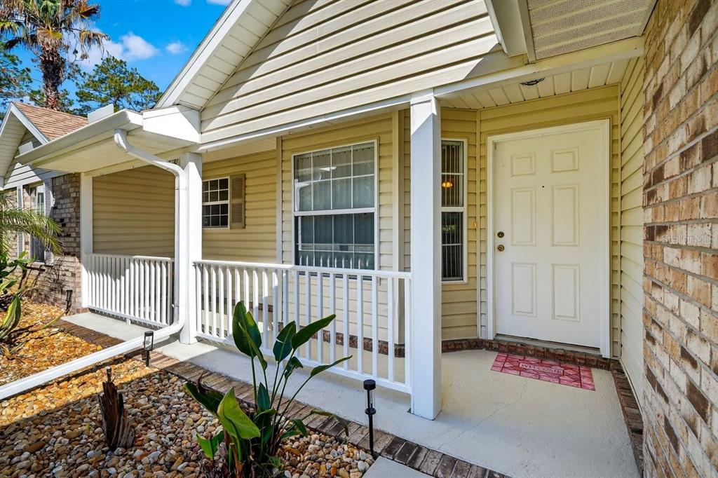 A tan-sided house exterior features a covered front porch, a white door, and rock landscaping — 89 ROBINSON DRIVE, PALM COAST, FL