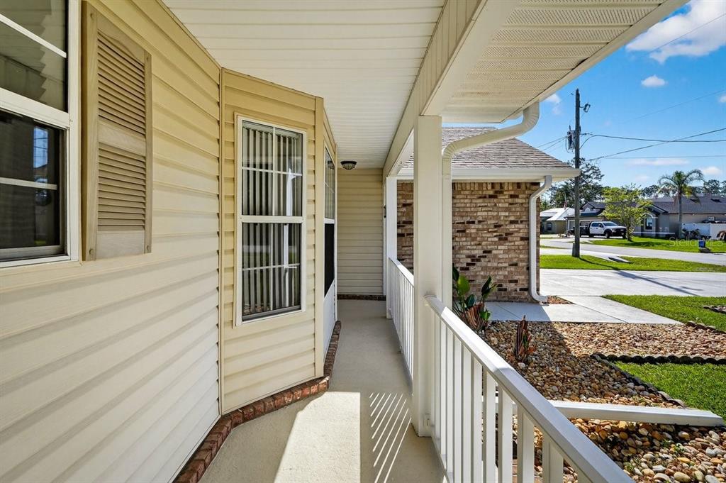 A covered front porch with beige vinyl siding, white railings, and a concrete floor — 89 ROBINSON DRIVE, PALM COAST, FL