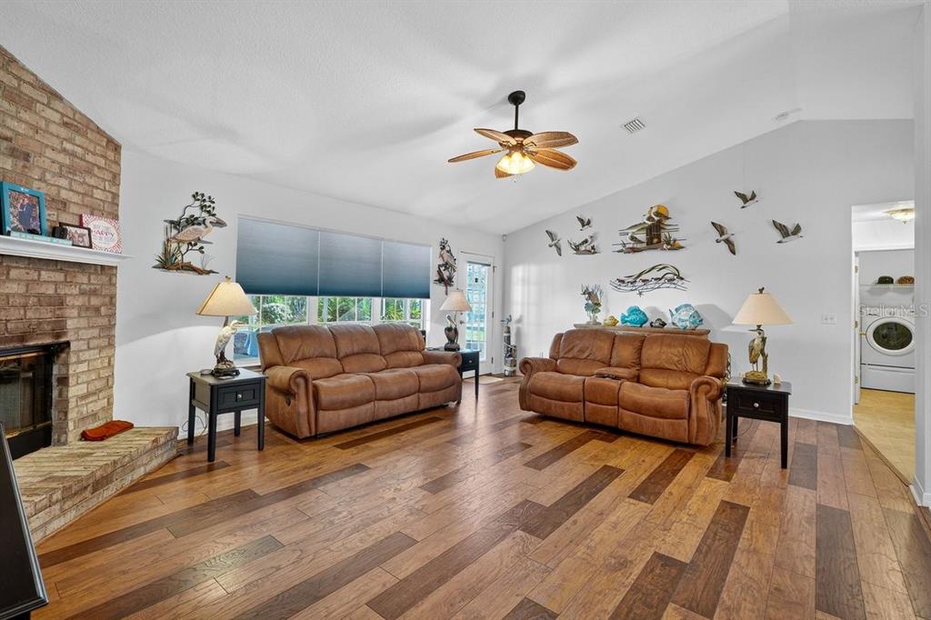 A living room with wood floors, two brown sofas, a brick fireplace, and vaulted ceilings — 89 ROBINSON DRIVE, PALM COAST, FL