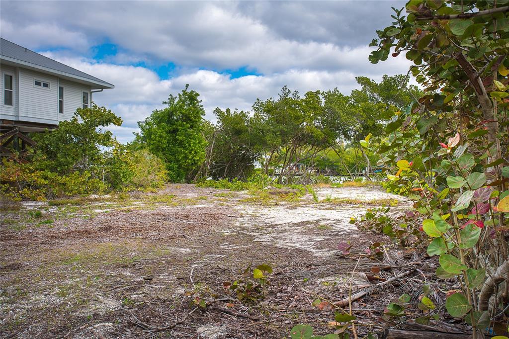 A vacant, sandy lot with sparse vegetation sits next to an elevated house under cloudy skies — 270 S GULF BOULEVARD, PLACIDA, FL