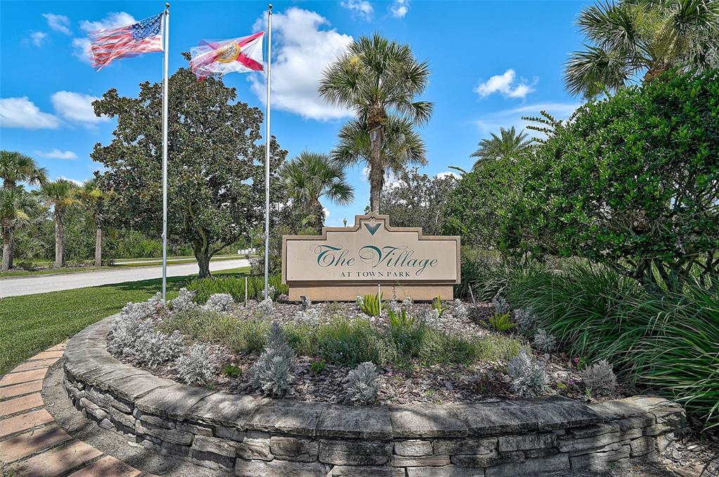 A stone sign for The Village at Town Park stands in a landscaped garden area — 8827 MANOR LOOP UNIT 204, LAKEWOOD RANCH, FL