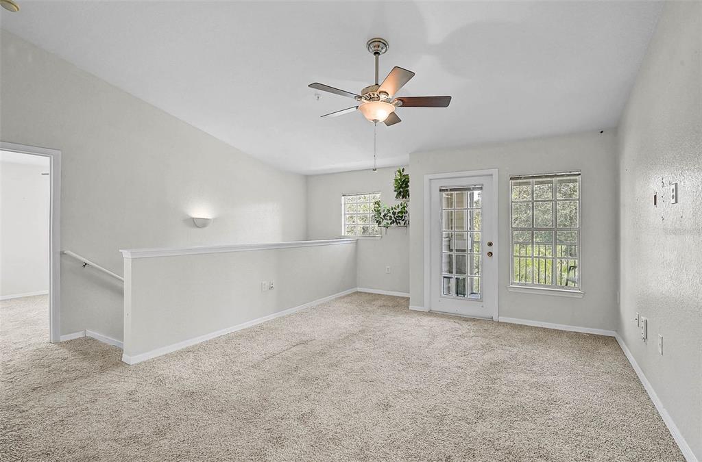 A carpeted loft area features a ceiling fan, a glass-paned door, and a staircase railing — 8827 MANOR LOOP UNIT 204, LAKEWOOD RANCH, FL