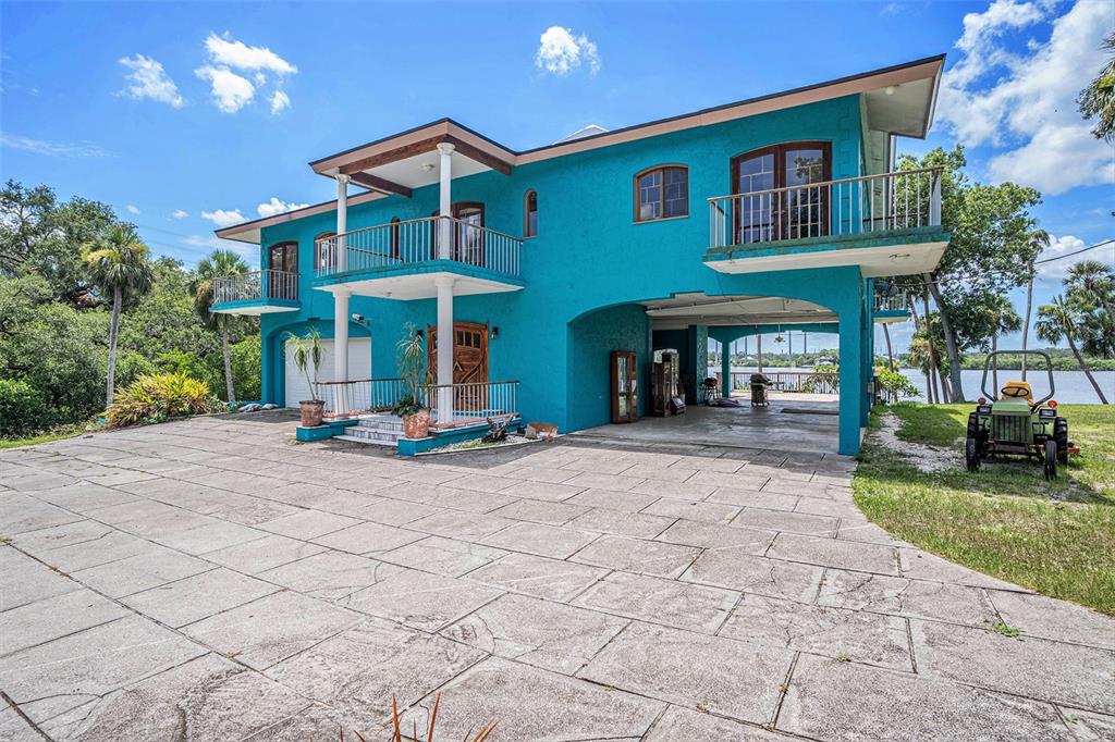 A bright blue two-story house with a large concrete driveway and a waterfront view — 7715 RIVERVIEW DRIVE, RIVERVIEW, FL