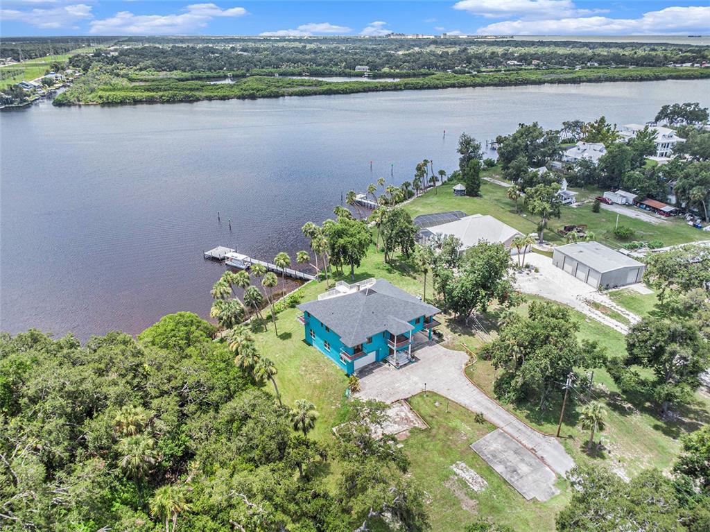 An aerial view shows a bright blue house with a dark roof near a river — 7715 RIVERVIEW DRIVE, RIVERVIEW, FL