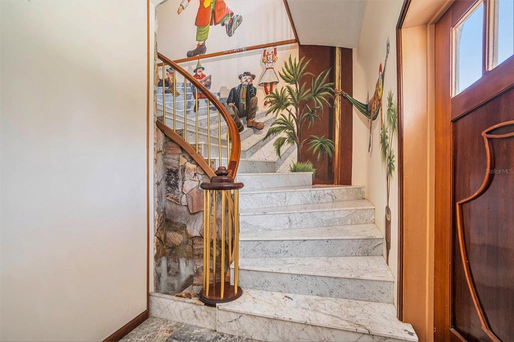 A marble staircase features a gold railing and walls painted with a clown mural — 7715 RIVERVIEW DRIVE, RIVERVIEW, FL