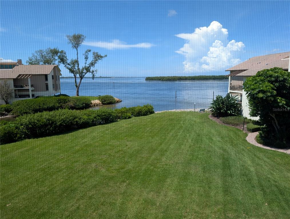A grassy lawn overlooks a body of water between two residential buildings — 3850 MARINERS WALK UNIT 723, CORTEZ, FL